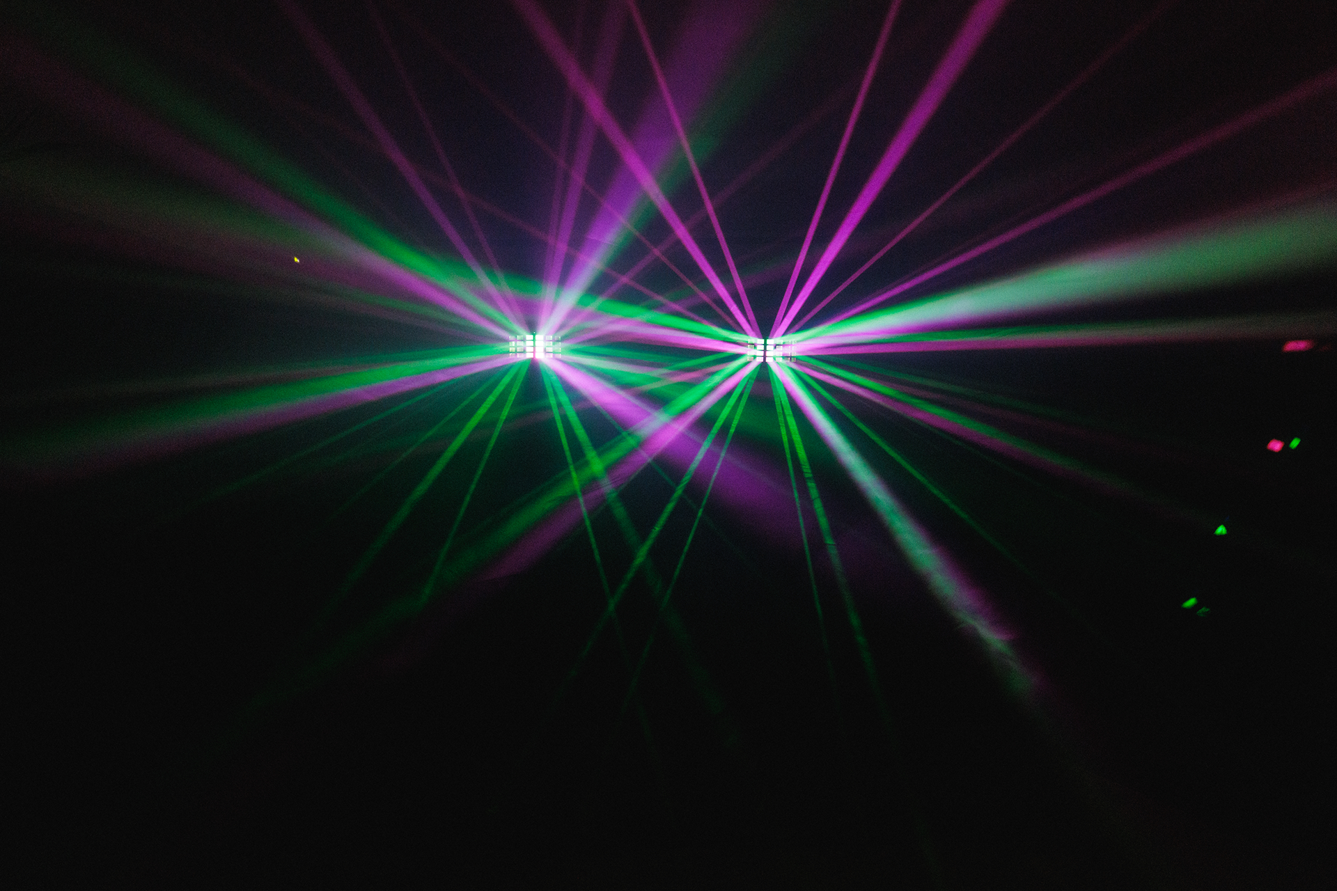 Två Derby-ljuseffekter projicerar gröna och lila strålar genom rökeffekter, vilket skapar ett dynamiskt ljusmönster i rummet.